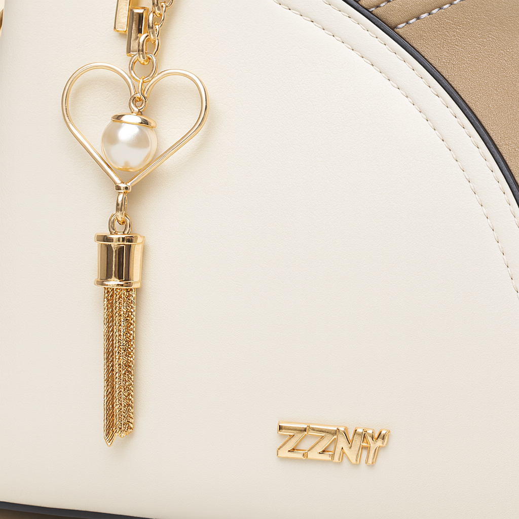 Ivory and taupe two-tone faux leather tote bag with gold-tone hardware, dual top handles, detachable crossbody strap, and heart-shaped charm with pearl accent.